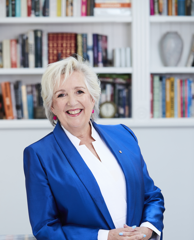 Smiling woman in a blue blazer poses in front of a bookshelf filled with books.
