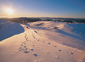 Snow-covered landscape with footprints along a path toward the horizon at sunset on a quiet winter day.
