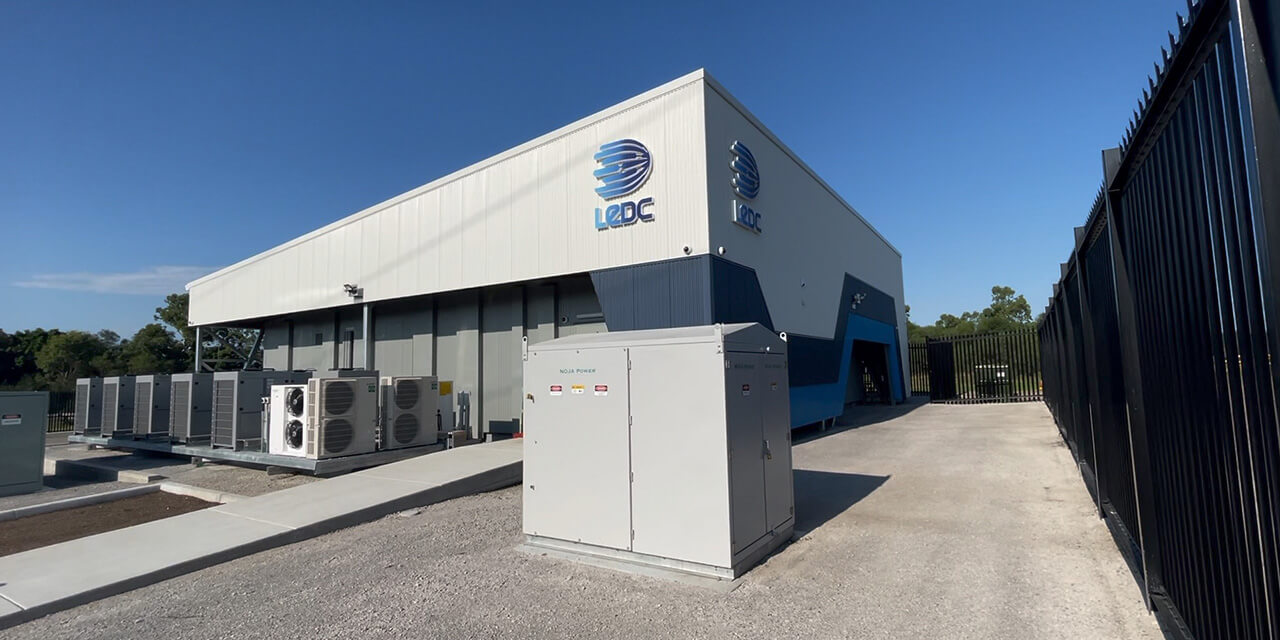 Exterior view of an industrial facility with LEDC logos, row of outdoor cooling/heating units, and a large electrical cabinet in the foreground.